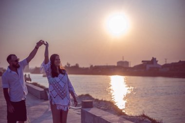 Hamile çift gün batımında platformda dans ediyor.