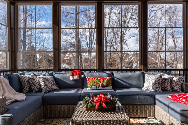 Уютная зима на крыльце во время праздников, снежные крыши и лес на заднем плане.