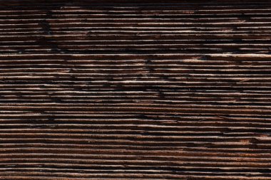 Old and weathered dark brown cracked wood beam surface with nice rough grain texture.