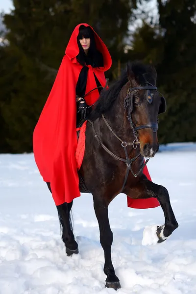 Krásná žena s červeným pláštěm s koněm venkovní v zimě — Stock fotografie