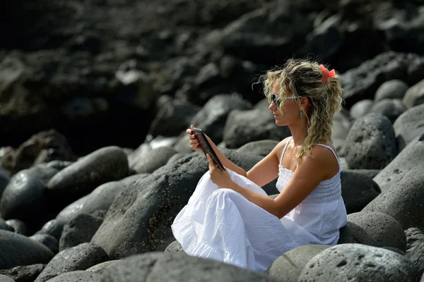 Młoda kobieta za pomocą tabletki na kamienistej plaży — Zdjęcie stockowe