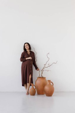 Hamilelik, geçmişi boş bir stüdyo. Beyaz arka planda bordo bir elbise giymiş güzel hamile bir kadın..