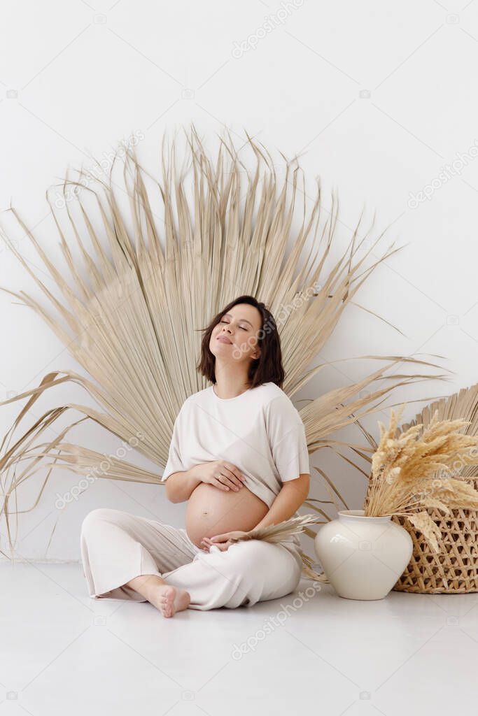A young pregnant girl in eco-style, on a white empty background. Smiling pregnant woman in boho style.