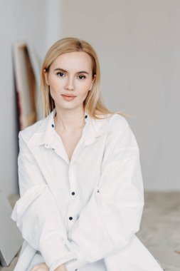 Bir fotoğraf stüdyosundaki kumda bir kız oturuyor. Genç bir sanatçı stüdyoda bir resim çiziyor..