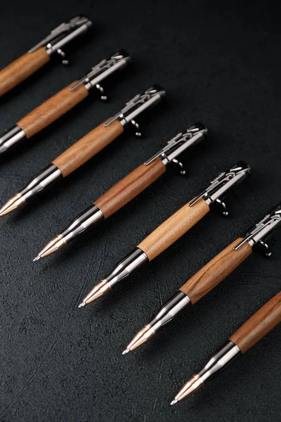 Μια σειρά από ακριβά στρατιωτικά στυλό φτιαγμένα από σπάνιο ξύλο, συνθέσεις σε σκούρο φόντο με χαρακτηριστικά. Πολυτελές στυλό δώρο. — Φωτογραφία Αρχείου