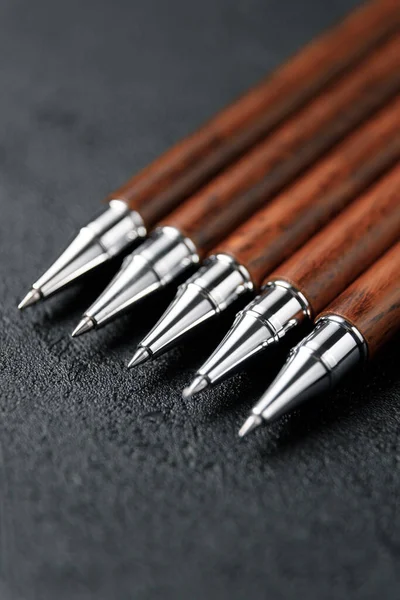 Un conjunto de costosas plumas militares hechas de madera rara, composiciones sobre un fondo oscuro con atributos. Bolígrafo regalo lujo. Fotos De Stock Sin Royalties Gratis