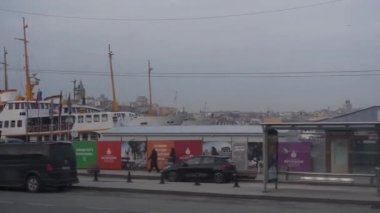 Limana yakın taksiler, inşaat alanı arkada, sağdan sola kayan insanlar ve binalar.