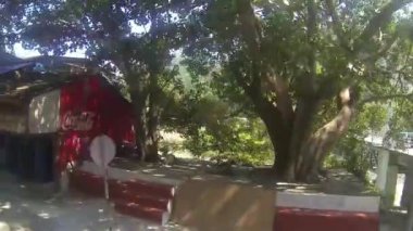 Renkli evlerin, arabaların ve su kaynağının önündeki elektrik hatlarının yanından geçerken arkada dağlar sağdan sola kayıyor. 