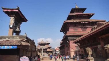 Etrafı anıtlarla çevrili sokakta yürüyen insanlar aşağı doğru eğiliyor. 