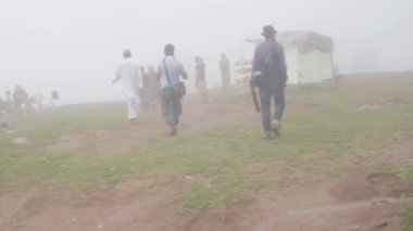 Men Walking And Sitting Down In Foggy Field