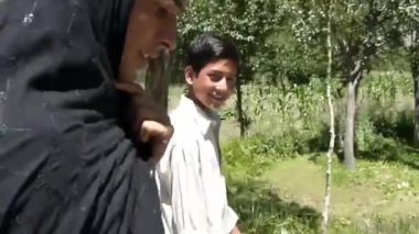 Boy And Man With Black Scarf Walking On Road Between Trees - Pan - Left To Right
