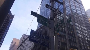 Road Direction Sign In Front Of Buildings From Below - Slide Right To Left And Pan Left To Right