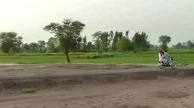 Passing By People On Motorbike Near Field With Flora - Slide - Left To Right