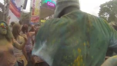 Man Covered By Green Colored Powder Jumping And Dancing In Crowd In Front Of Stage - Pan Left To Right, Then Right To Left.