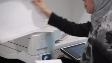 Fotokopi makinesinden kaçan gri tesettürlü kadın işçi.