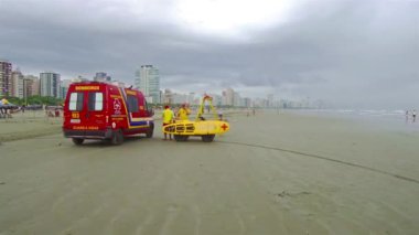 Sahilde gözcülük yapan cankurtaranlarla birlikte kırmızı ambulans ve kürekli tahtalar.
