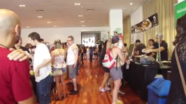 İnsanlar bir sergide farklı tezgahlara bakıp konuşuyorlar.