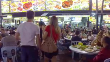 White couple walking to a table at a night market in malaysia