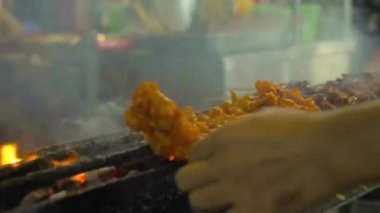 man placing bbq satay on sticks on a grill at a night market in kuala lumpur - over the shoulder
