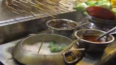 A hand putting sausages in a pot of boiling water at a steam boat stall at a night market