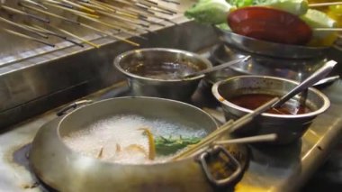 A hand putting sausages in a pot of boiling water at a steam boat stall at a night market