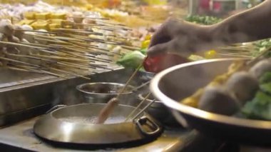 A man taking out sausages from a steam boat pot to his plate at a night market