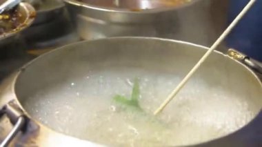  Gece pazarındaki buharlı tekne tezgahında kaynamış bir su kabına sebze koyan bir adam.