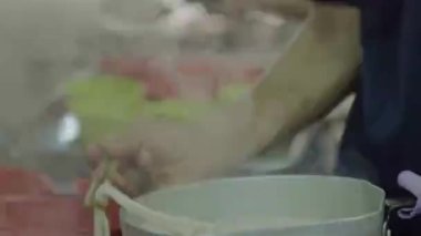 Asian guy preparing dry noodles with soup in red bowls