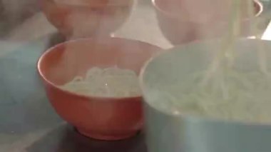  Asian guy putting dry noodles with soup in red bowls with chopsticks