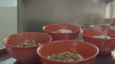 Asian guy putting hot eggs on top of a red beef noodle bowls