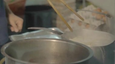 asian man cooking noodles in a big silver pot