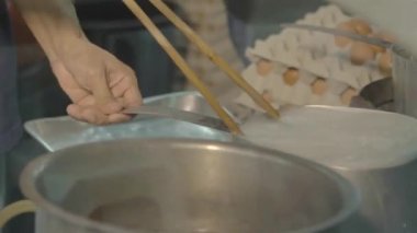 Malaysian man cooking noodles in a big silver pot - side view