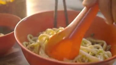 Biber ve erişteyi yemek çubuğu ve kaşıkla karıştıran kişi.