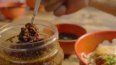  Kuru eriştenin üstüne kaşık dolusu kırmızı biber koyan kişi..