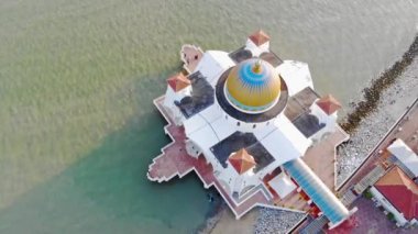 Deniz kenarındaki güzel beyaz bir camide insanların görüntüsü ve küçük dalgalar soldan sağa doğru dönüyor.