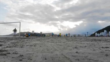 İnsanlar Santos Sahili 'nde sarı ve mavi tişörtlü futbol oynuyorlar..