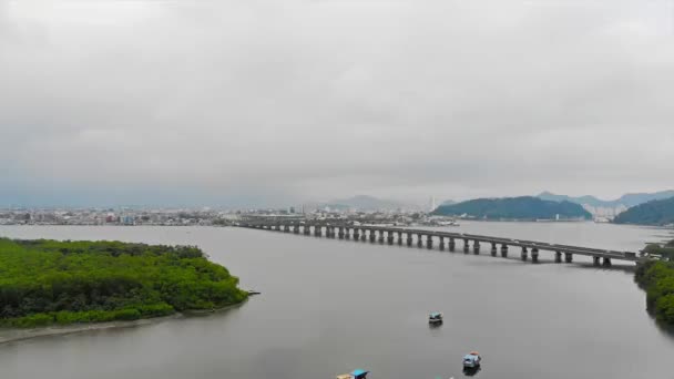 サントスと橋の街の景色を望む木々でいっぱいの島の近くのカラフルな漁船の空中ビュー — ストック動画