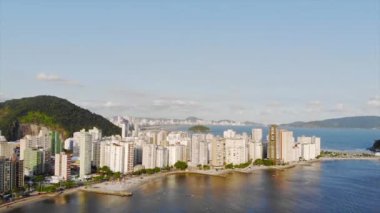  Santos şehri ve dağın bulunduğu denizin yakınındaki yeşil bir adada gökdelenlerin manzarası var.