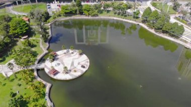Top Aerial View Of Green Lake With Roundabouts And Reflections Near Buildings - Dolly Left To Right.