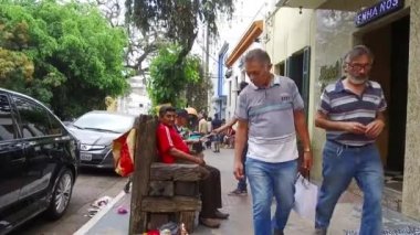 Yol kenarındaki tahta sandalyede oturan kırmızı tişörtlü yaşlı bir adam..