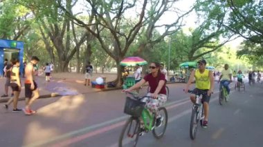 Mavi binaların önünde birlikte bisiklete binen insanlar Dolly Sağdan Sola.