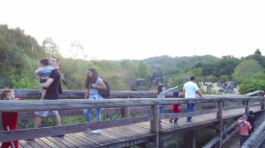 Ziyaretçiler parkları ve gölleri gören tahta bir köprüde soldan sağa doğru hareket ediyorlar.