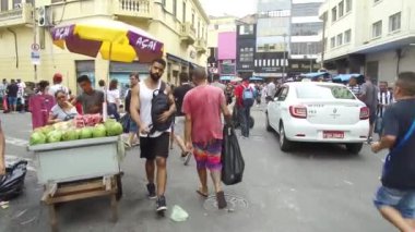 Dükkanlar arasında bir cadde dolusu yaya ve tüccar - İleri - Sağdan Sola.