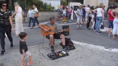  Kara Gömlekli Küçük Bir Çocuk Sokak Müzisyeninden Gitar Performansını İzliyor.
