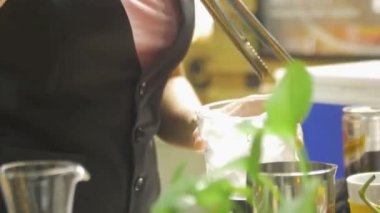 Kadın maşayla bardaktan buz topluyor.