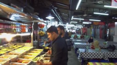 Sıraya dizilmiş yemek tezgahları ve yan taraftaki masalar.