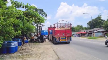 Gün boyunca yol kenarında Mavi Fıçıları boşaltan Kırmızı Kamyon - Geniş