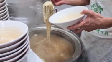 Taze pişirilmiş el yapımı erişteler yemek çubukları tarafından toplanıp çorba kasesine konur.