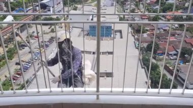 Balkonda asılı bir adam bir apartmanın duvarlarını boyuyor. 
