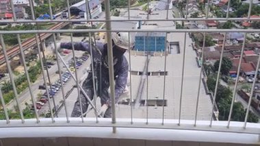 Balkonda asılı duran uzun bir binanın duvarını boyayan adam.